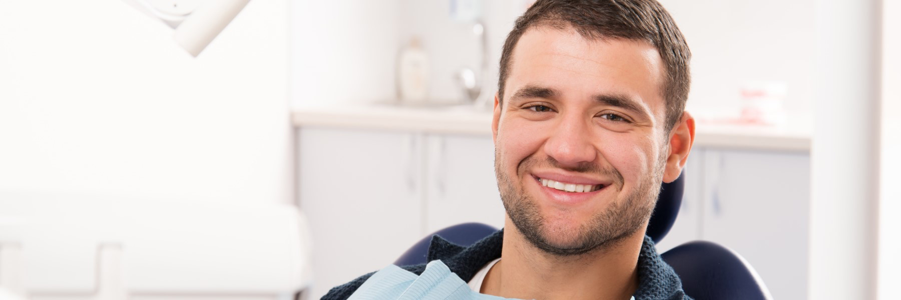 Smiling man wearing a dental bib seated in a dental chair after filling treatment