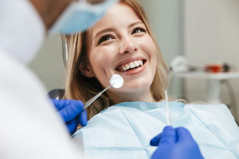 A woman smiles happily while sitting in a dentist chair, showcasing a positive dental experience.