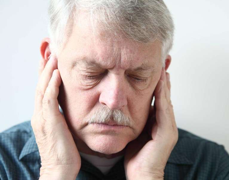 A man grimaces, clutching his ear in pain from a TMJ-related earache.